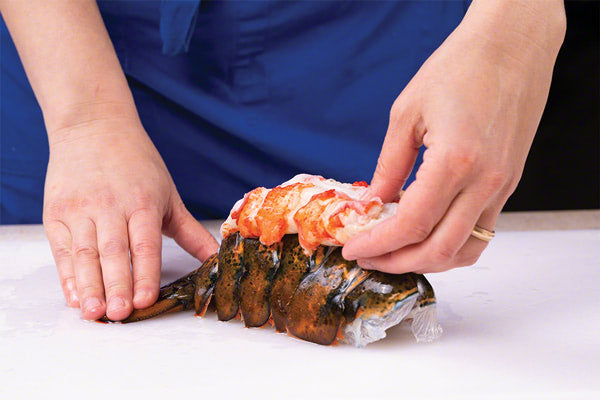 Hands resting loosened lobster tail meat on top of the shell