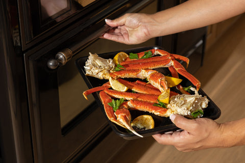 Snow crab clusters in a roasting pan with lemon and herbs, being placed in the oven